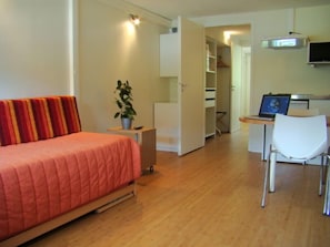 A compact bedroom with a bed, a small desk, a chair, and a potted plant.