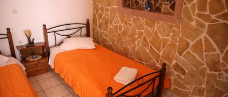 Un dormitorio con dos camas individuales, una pared de piedra y un estante con adornos.