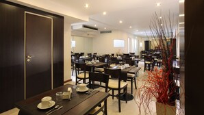 Uma sala de jantar de hotel com várias mesas e cadeiras, uma porta de madeira escura e uma planta decorativa.