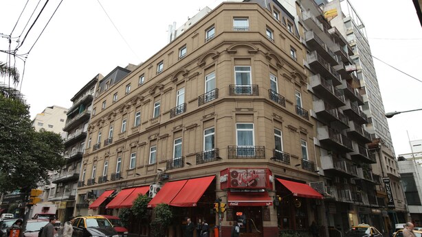 Um edifício com canto, toldo vermelho, várias sacadas e um anúncio da Coca-Cola.