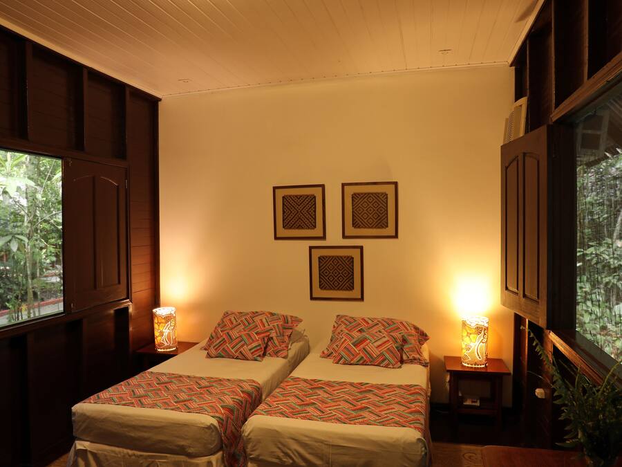 Une chambre avec deux lits, une fenêtre donnant sur un paysage verdoyant et des œuvres d’art décoratives sur les murs.