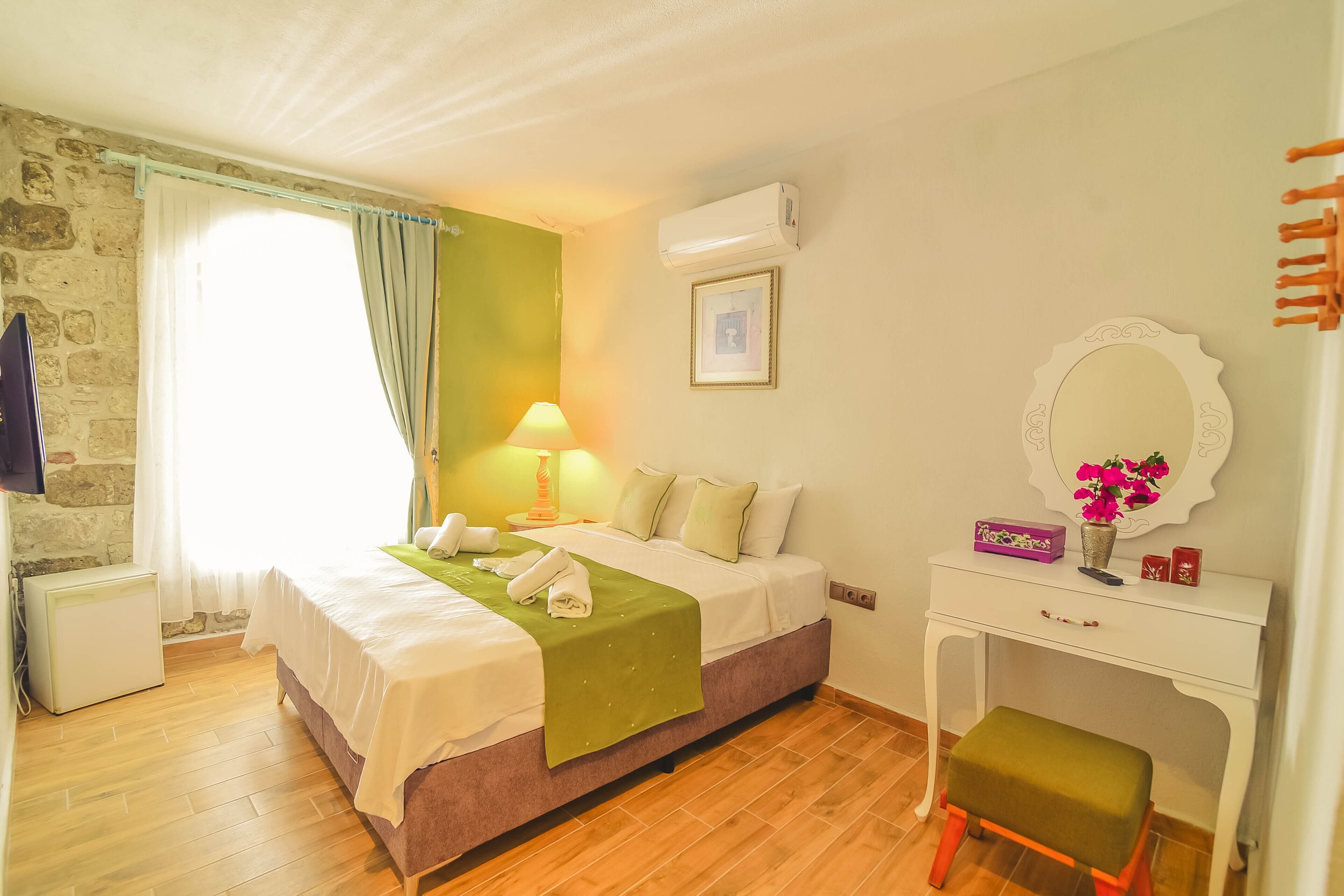 A bedroom with a bed, bedside table, lamp, air conditioning unit, and a small stool.