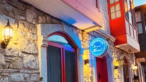 A stone building with a red door and windows, a neon sign reading "Bedirhan Hotel," and outdoor seating with red chairs and a table.