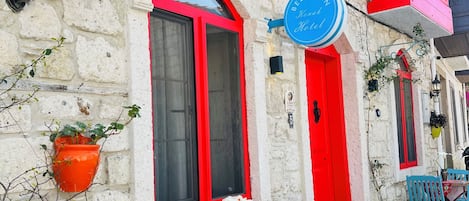 A stone building with red-framed windows and doors, a signboard, and a table with red chairs.