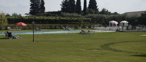 Area piscina con lettini e ombrelloni, circondata da vegetazione e alberi.