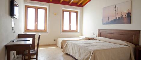 A bedroom with two beds, a desk, and a chair. There are two windows and a painting on the wall.