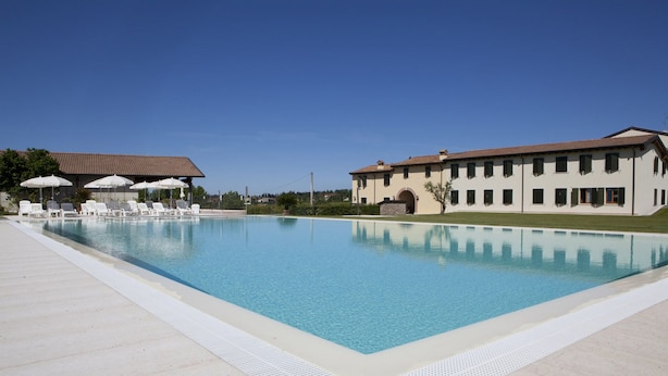A rectangular swimming pool with lounge chairs and umbrellas, surrounded by a paved deck. - Corte Pontigliardo (Lazise)