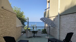 A balcony with a view of the sea, furnished with two chairs, a table, and an umbrella.