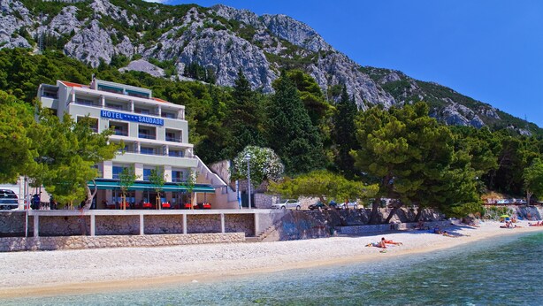 A hotel with a stone facade, multiple balconies, and a beach view.