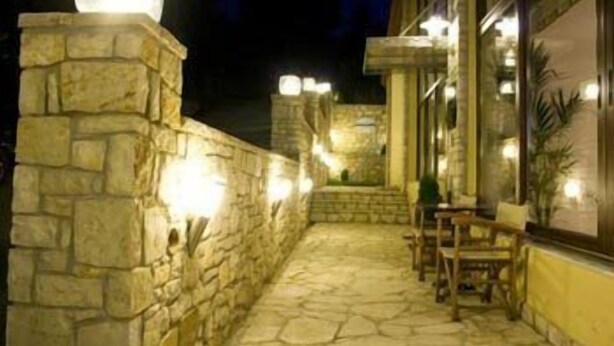 A stone-walled outdoor area with a seating arrangement and a staircase leading to an upper level. - Ahilion (Kalavrita)