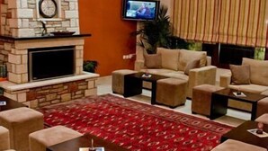 A living room with a stone fireplace, beige sofas, a red patterned rug, and a television mounted on the wall. - Ahilion (Kalavrita)