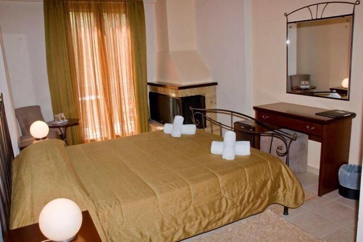 A hotel room with a bed, a bedside table, a mirror, a desk, and a trash bin.