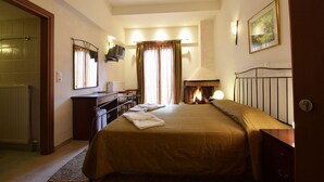 A hotel room with a bed, a desk, a chair, a fireplace, and a large window with curtains. - Ahilion (Kalavrita)