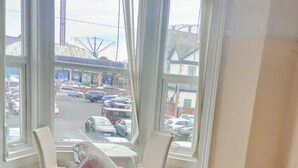 Une chambre d’hôtel dotée d’une grande fenêtre donnant sur un parking et une grande roue. On y trouve un canapé avec un coussin et une petite table à côté.