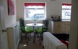 A small kitchen with a dining table, two chairs, a window with a view of a building, and a bed in the foreground. - Aparthotel Blackpool (Blackpool)