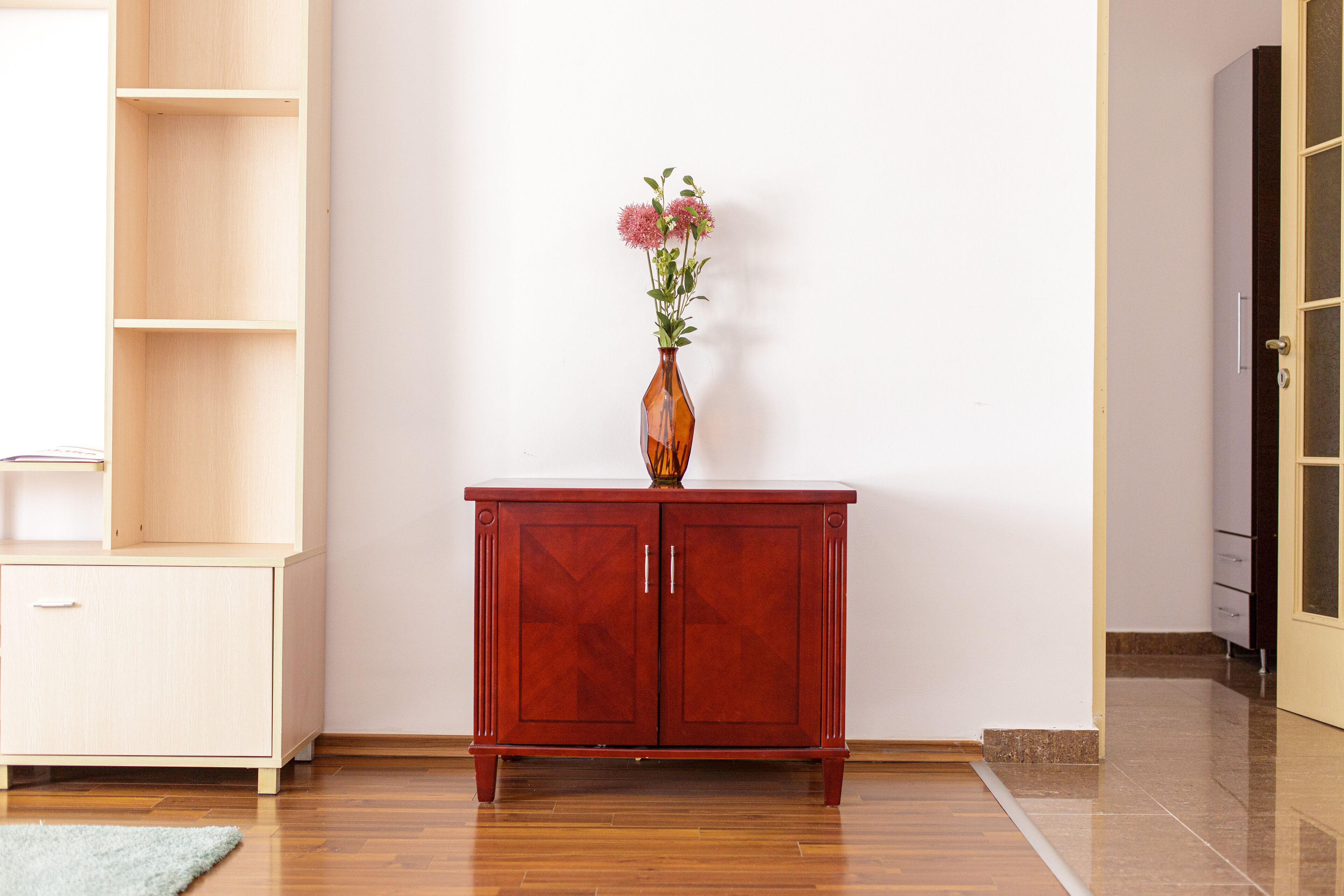 A wooden cabinet with two doors and a vase with flowers on top.