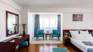 A hotel room with a bed, a desk with a chair, two armchairs, a small table with a plant, and a painting on the wall. - Lira Pacific Aparthotel (Constanta)