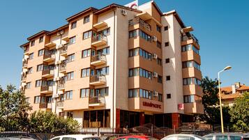 Un hotel de varios pisos con balcones, un letrero que dice "LIRAG PACIFIC" y varios coches estacionados al frente.