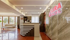 A modern hotel lobby with a reception desk, a sofa, and a large window offering a view of the city. - Lira Pacific Aparthotel (Constanta)