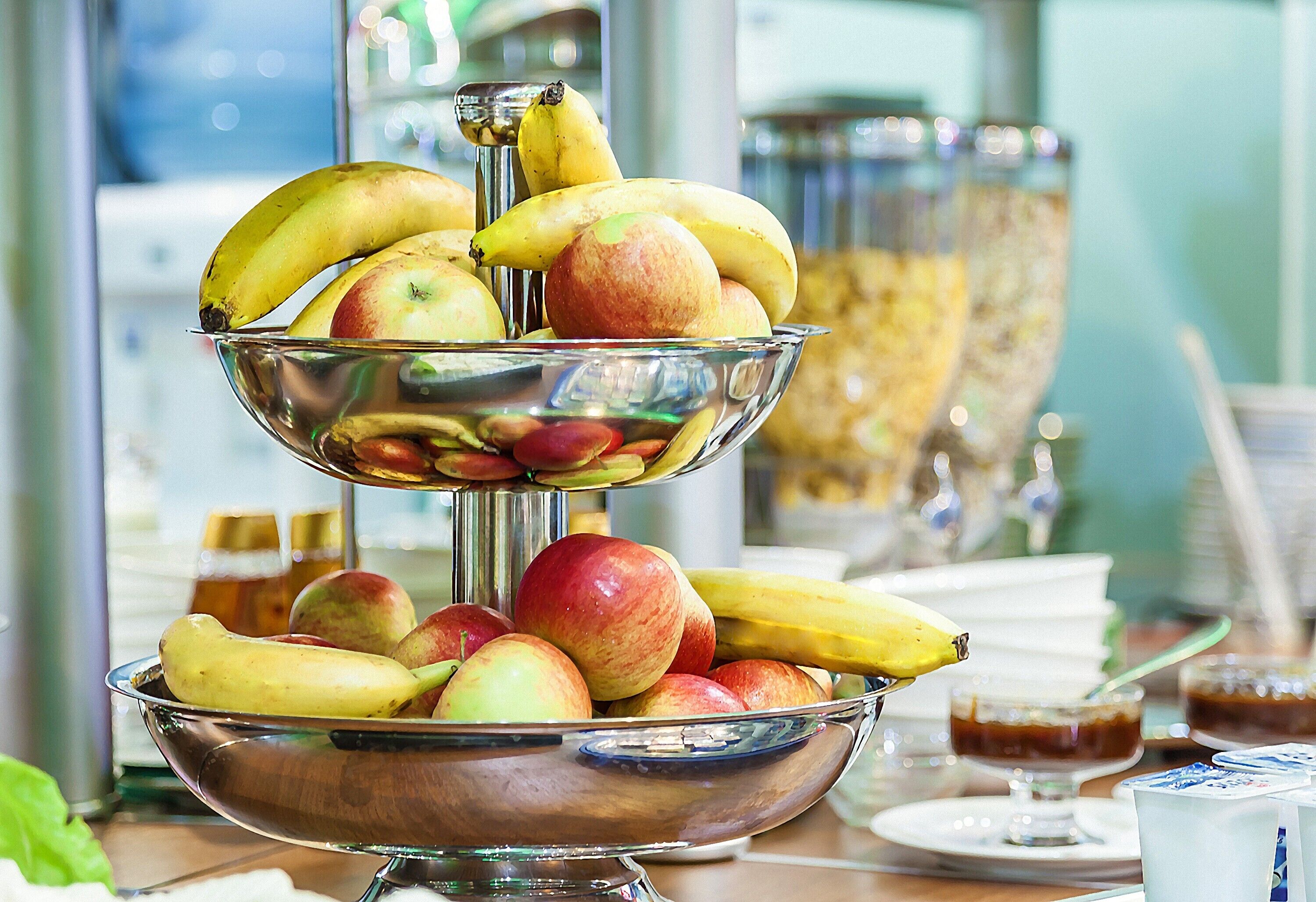 A three-tiered fruit bowl with bananas and apples on a table.