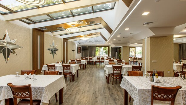 A spacious dining area with multiple tables and chairs, a modern chandelier, and a large star decoration on the wall. - Lira Pacific Aparthotel (Constanta)