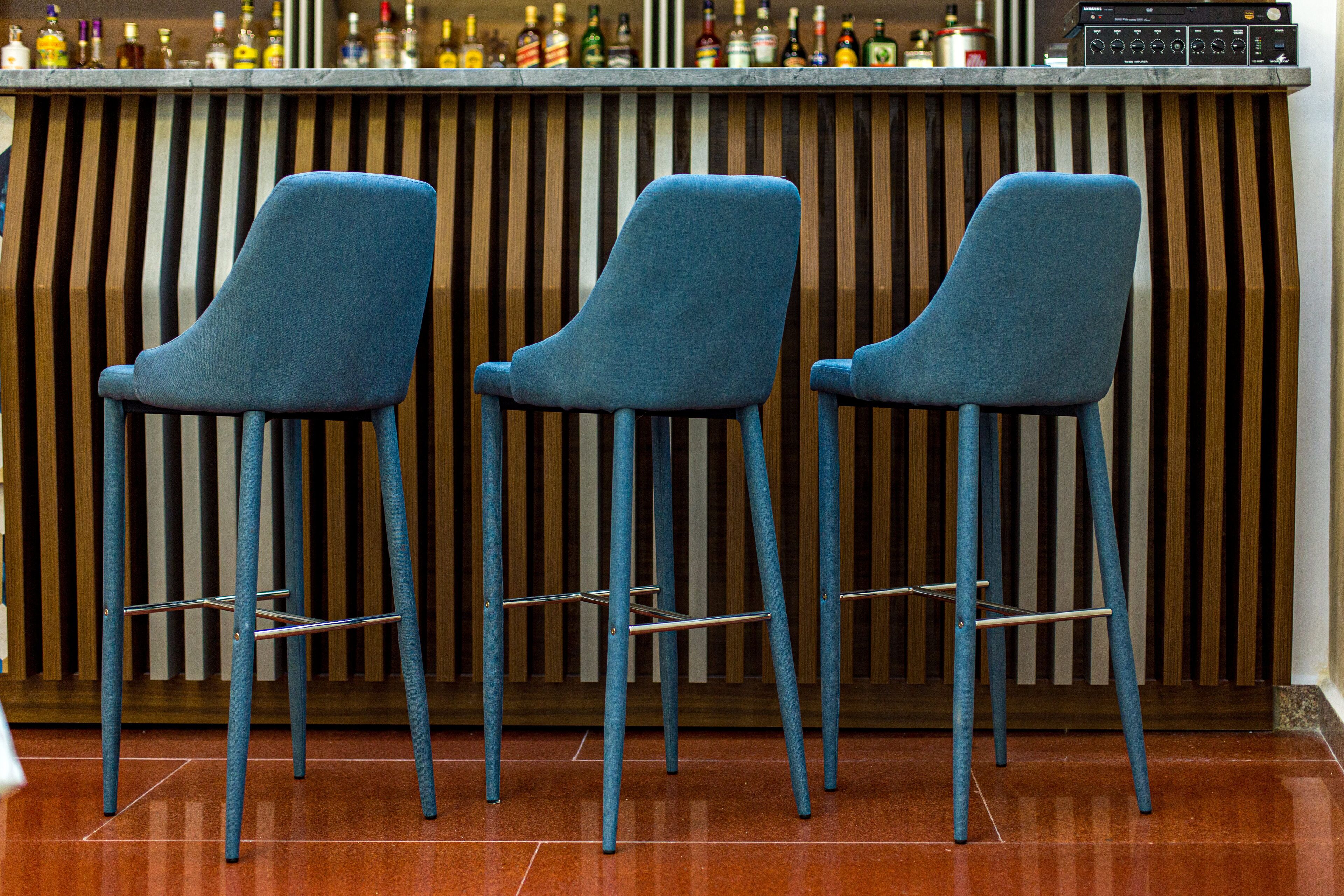 Tres taburetes azules con patas metálicas y una pared de listones de madera al fondo.