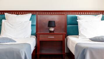 Habitación de hotel con dos camas, una mesita de noche con lámpara y cabeceros tapizados en color verde azulado.