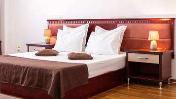 Una cama bien tendida con un cabecero marrón, dos mesitas de noche con lámparas y suelo de madera.