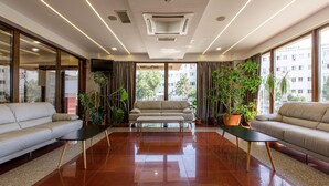 A modern hotel lobby with a sofa, a coffee table, and potted plants. - Lira Pacific Aparthotel (Constanta)