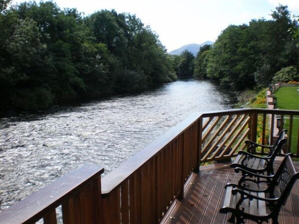 A wooden deck with a railing overlooking a river, surrounded by lush greenery and a mountain in the distance. - Crystal Springs B&B (Killarney)