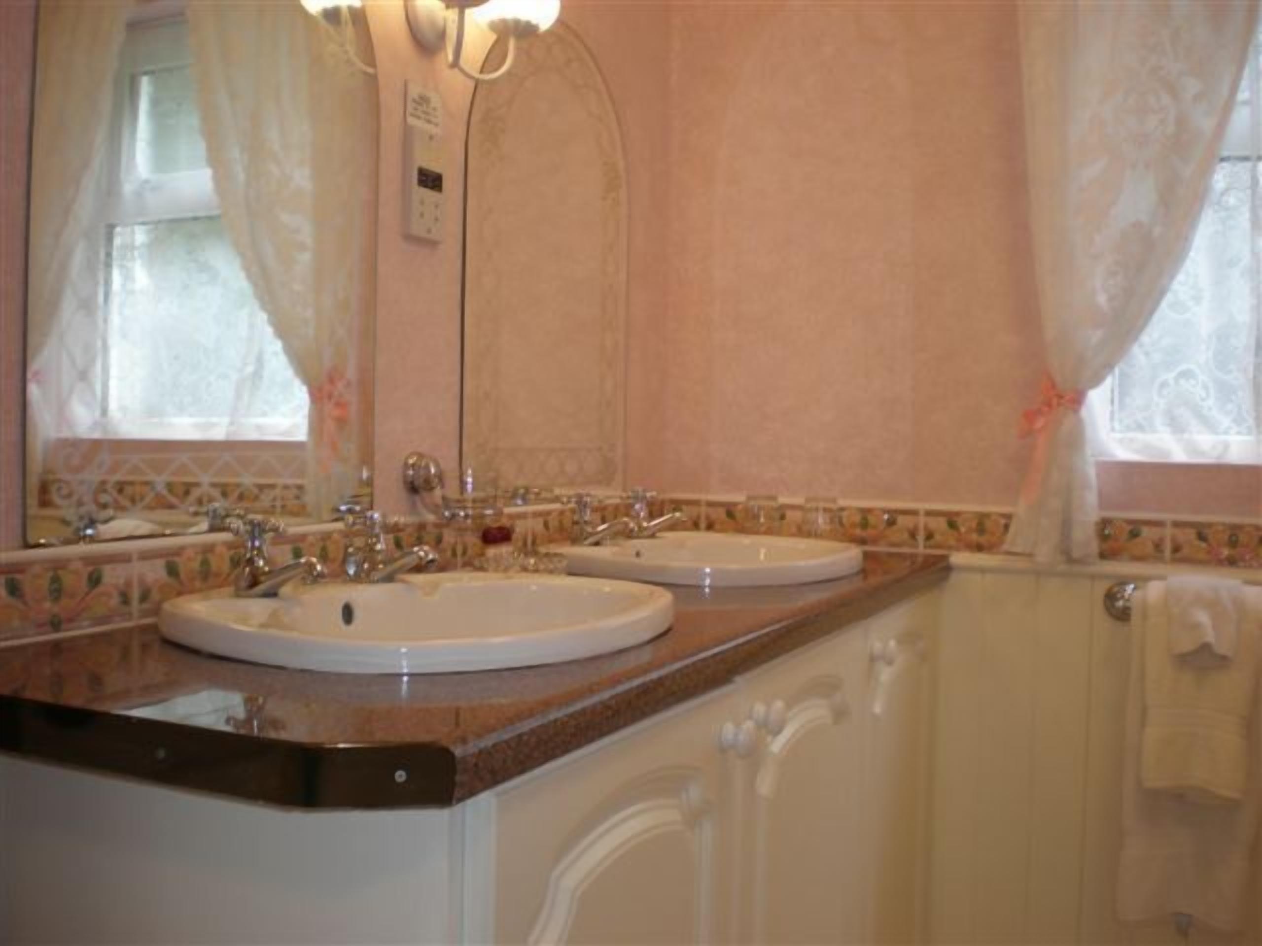 Un baño con dos lavamanos, un espejo y una ventana con cortinas.