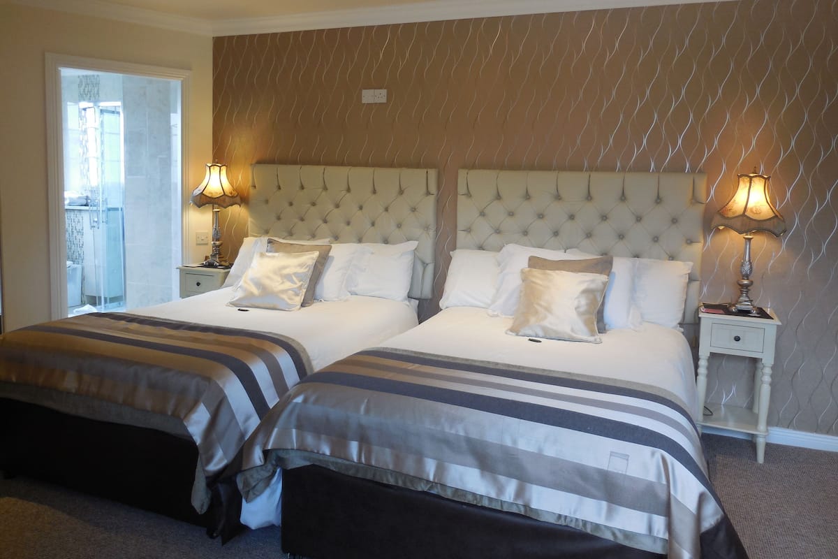 A hotel room with two beds, a large window, and a bathroom visible through the door.