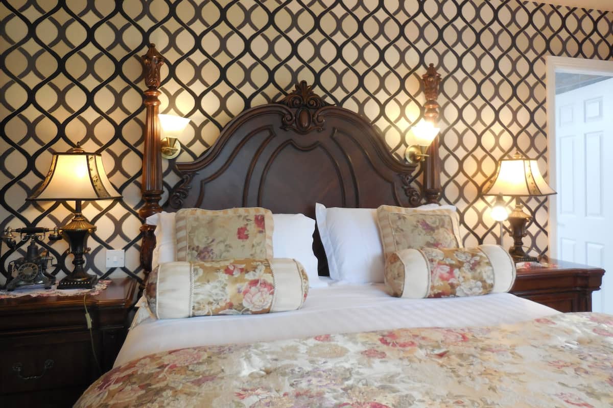 A bedroom with a patterned wallpaper, a wooden headboard, two bedside tables with lamps, and floral bedding.