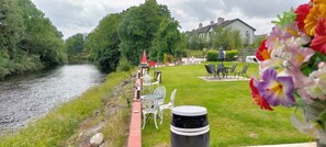 A riverside patio with outdoor seating, a table, and a flower arrangement. - Crystal Springs B&B (Killarney)