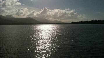 A calm lake with sunlight reflecting off the water's surface, surrounded by mountains and a partly cloudy sky.