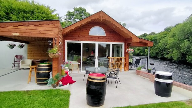 A wooden cabin with a patio, outdoor seating, and a river view.