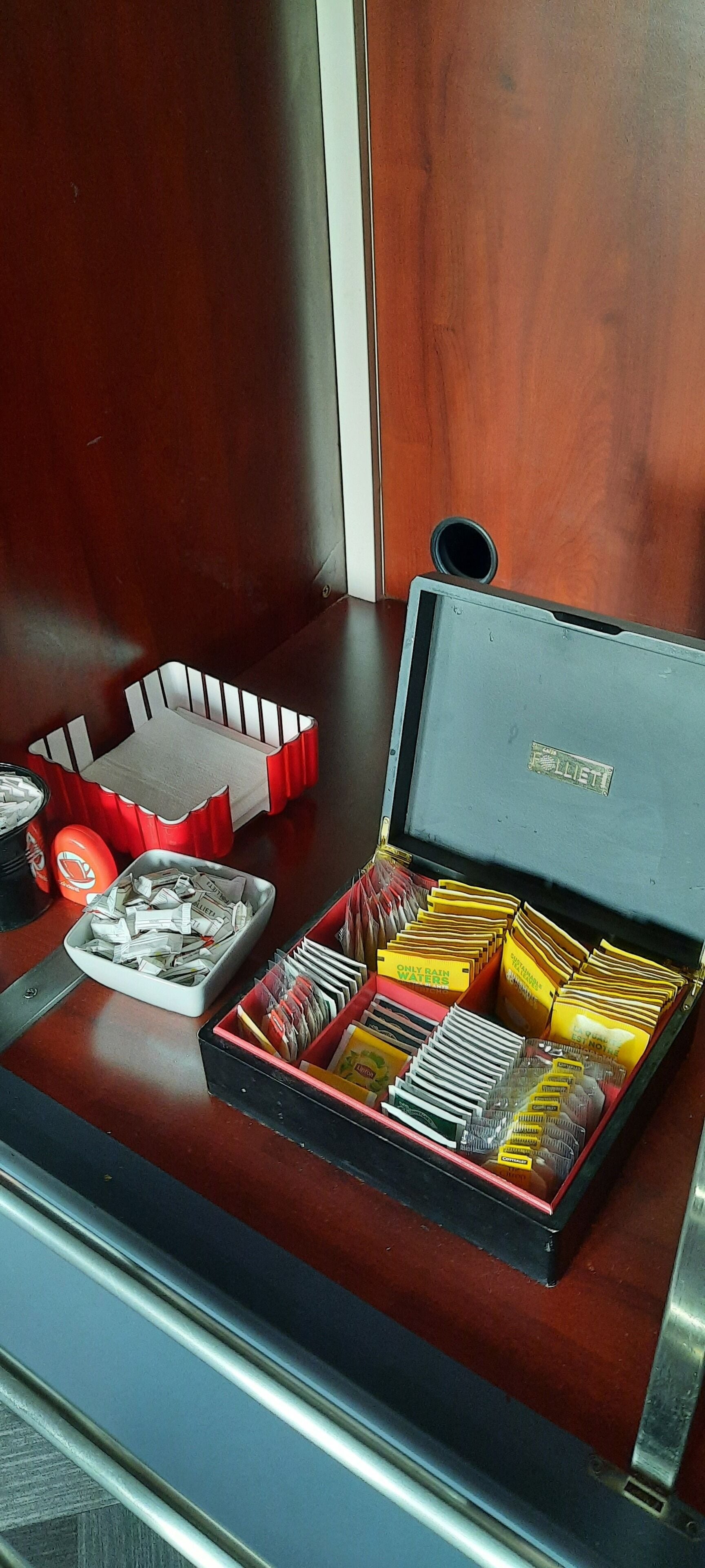 A wooden table with a red and black box containing various items, including a tray of packets and a small container.