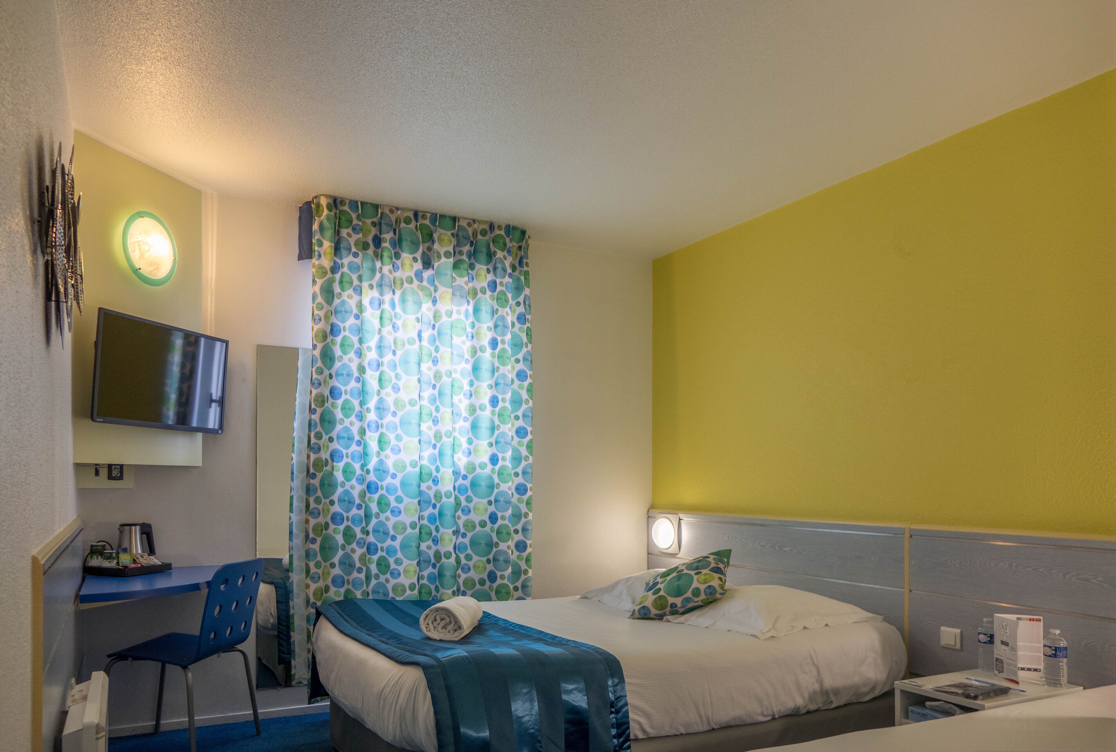 A hotel room with a bed, a desk, a chair, a television, and a curtain with a polka dot pattern.