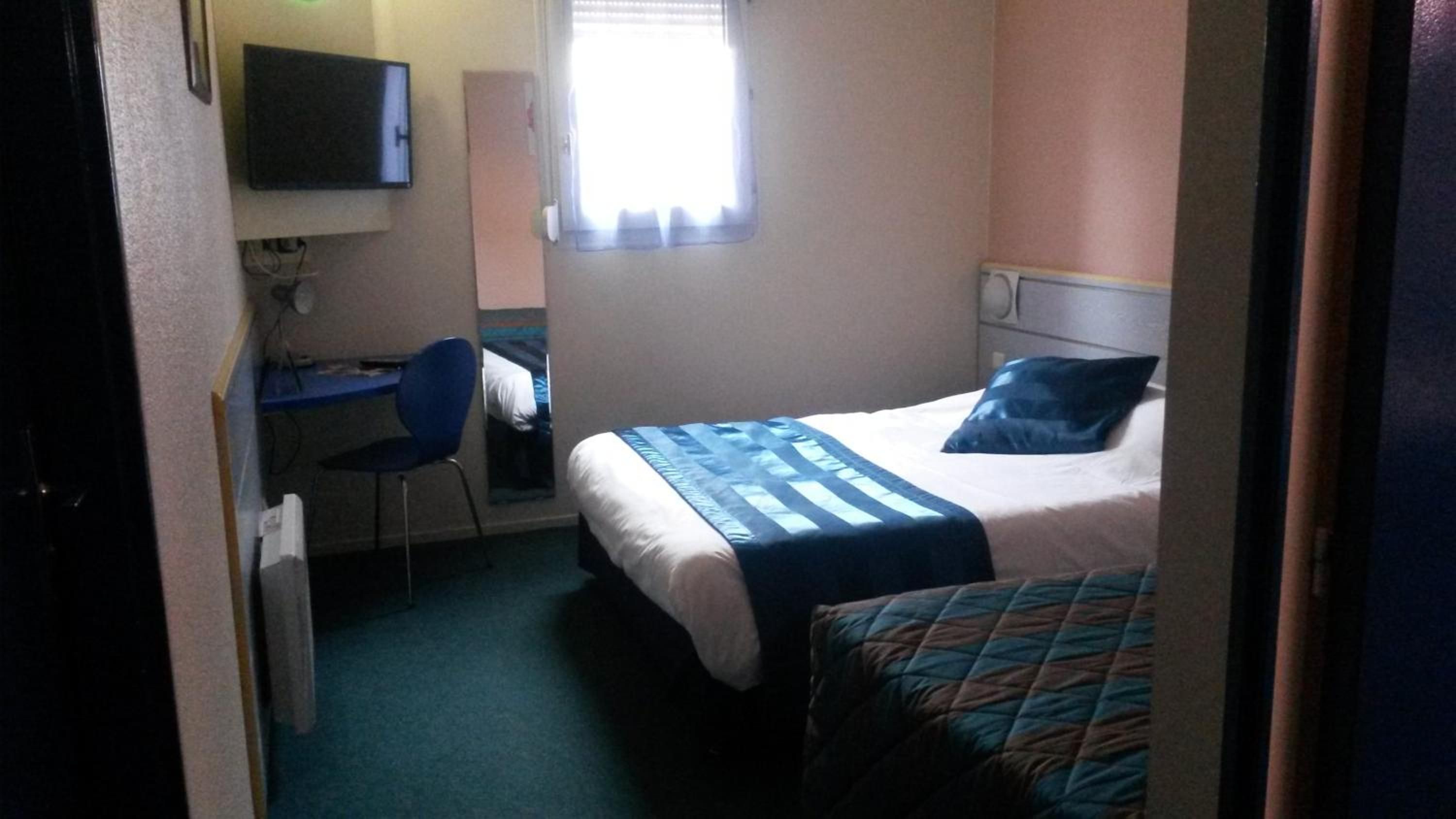 A hotel room with a bed, a desk, a chair, a television, and a window.