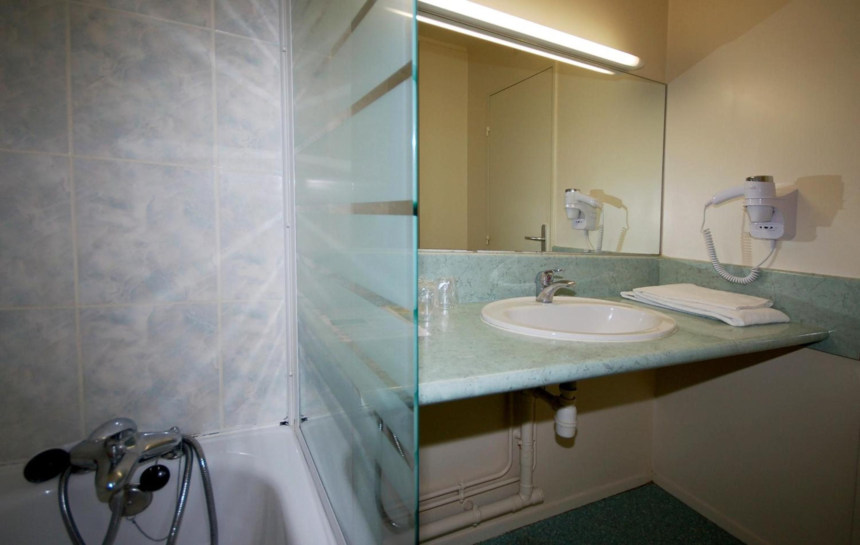 Ein Badezimmer mit einer Badewanne, einem Waschbecken, einem Spiegel und einem Föhn auf der Ablagefläche.