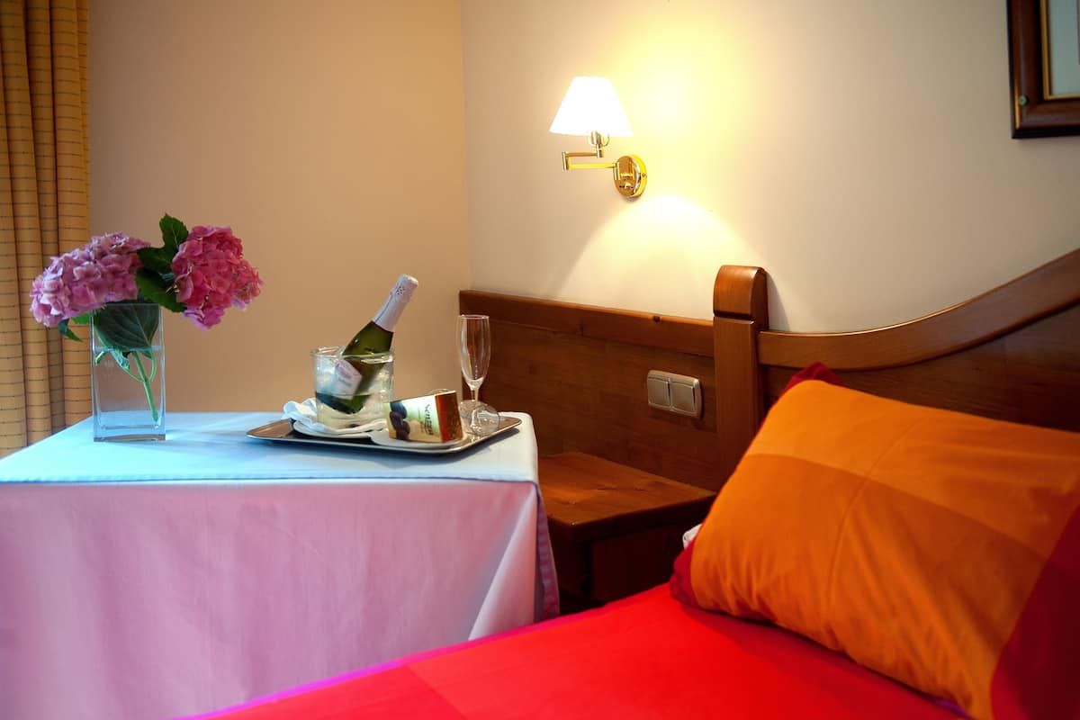 A hotel room with a bed, a bedside table with a bottle and glass, and a vase with flowers on the table.