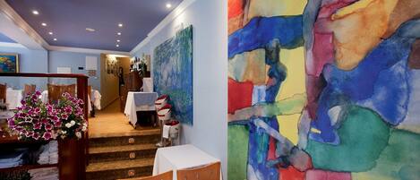 A hotel lobby with a staircase, a reception desk, and a large abstract painting on the wall.