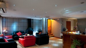 A modern hotel lobby with a reception desk, seating area with red and black sofas, a fireplace, and a staircase. - Hotel Montane (Arinsal)
