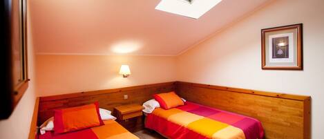 A small, cozy room with two single beds, a nightstand, a wall-mounted lamp, and a framed picture on the wall.