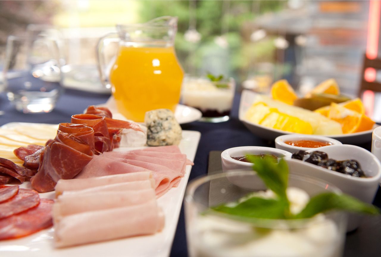 A breakfast buffet with various meats, cheeses, fruits, and beverages.