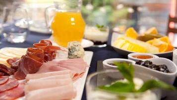 A breakfast buffet with various meats, cheeses, fruits, and beverages.