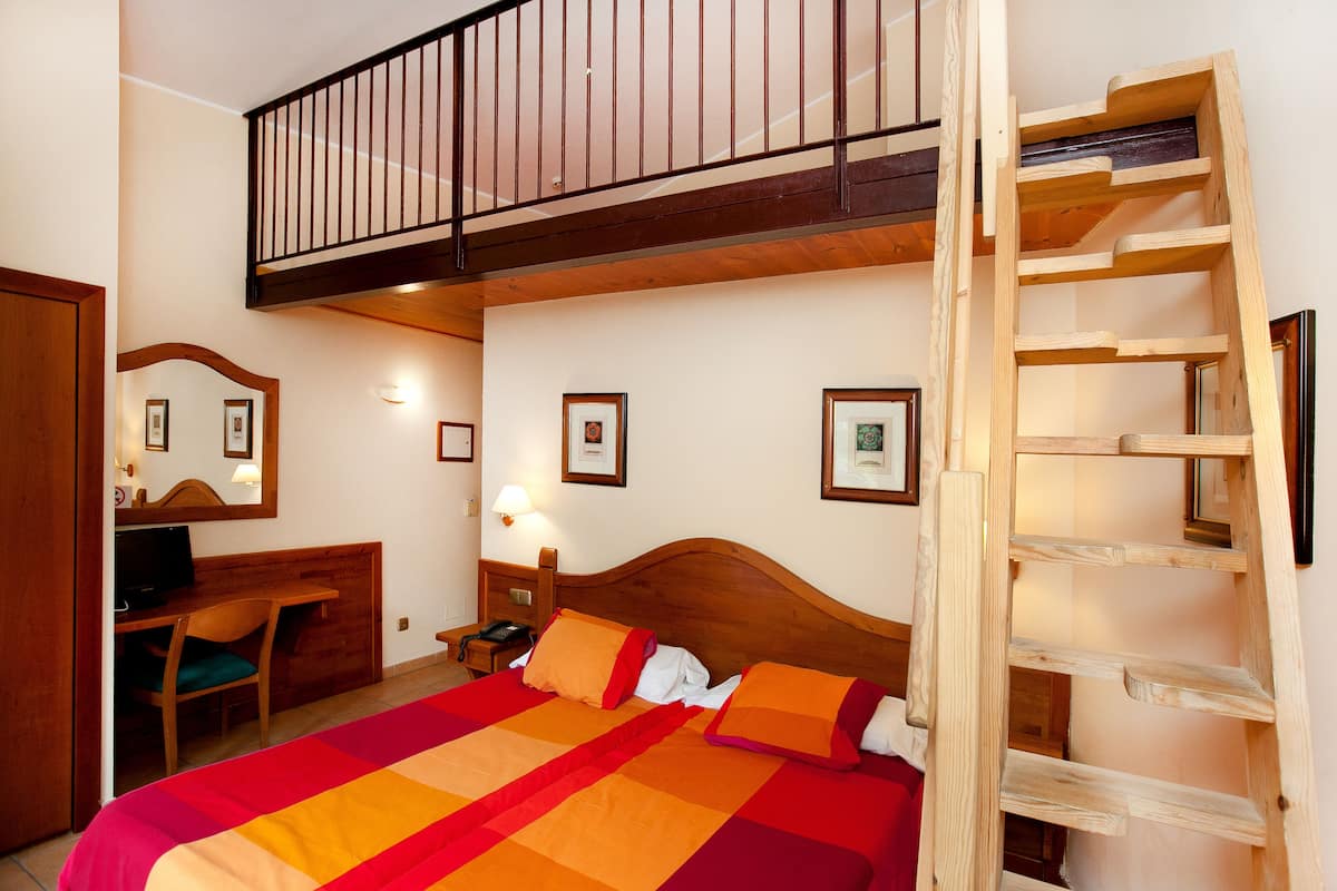 A bedroom with a wooden bed, a desk, a chair, a nightstand, a lamp, and a wooden ladder.