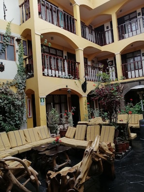 Un immeuble à plusieurs étages aux murs jaunes, doté de balcons avec des rampes en bois et d’espaces extérieurs aménagés avec des coussins et des tables.
