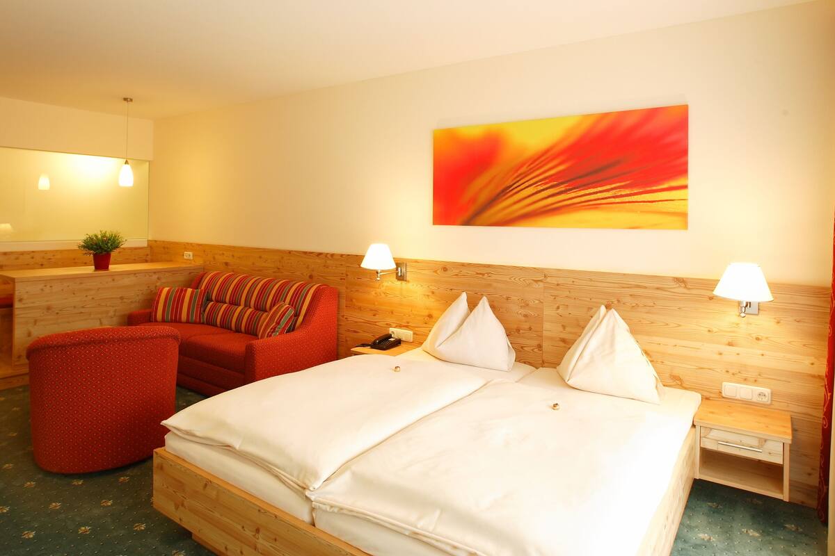 A hotel room with a wooden bed, a red armchair, a small desk, and a wall-mounted lamp.