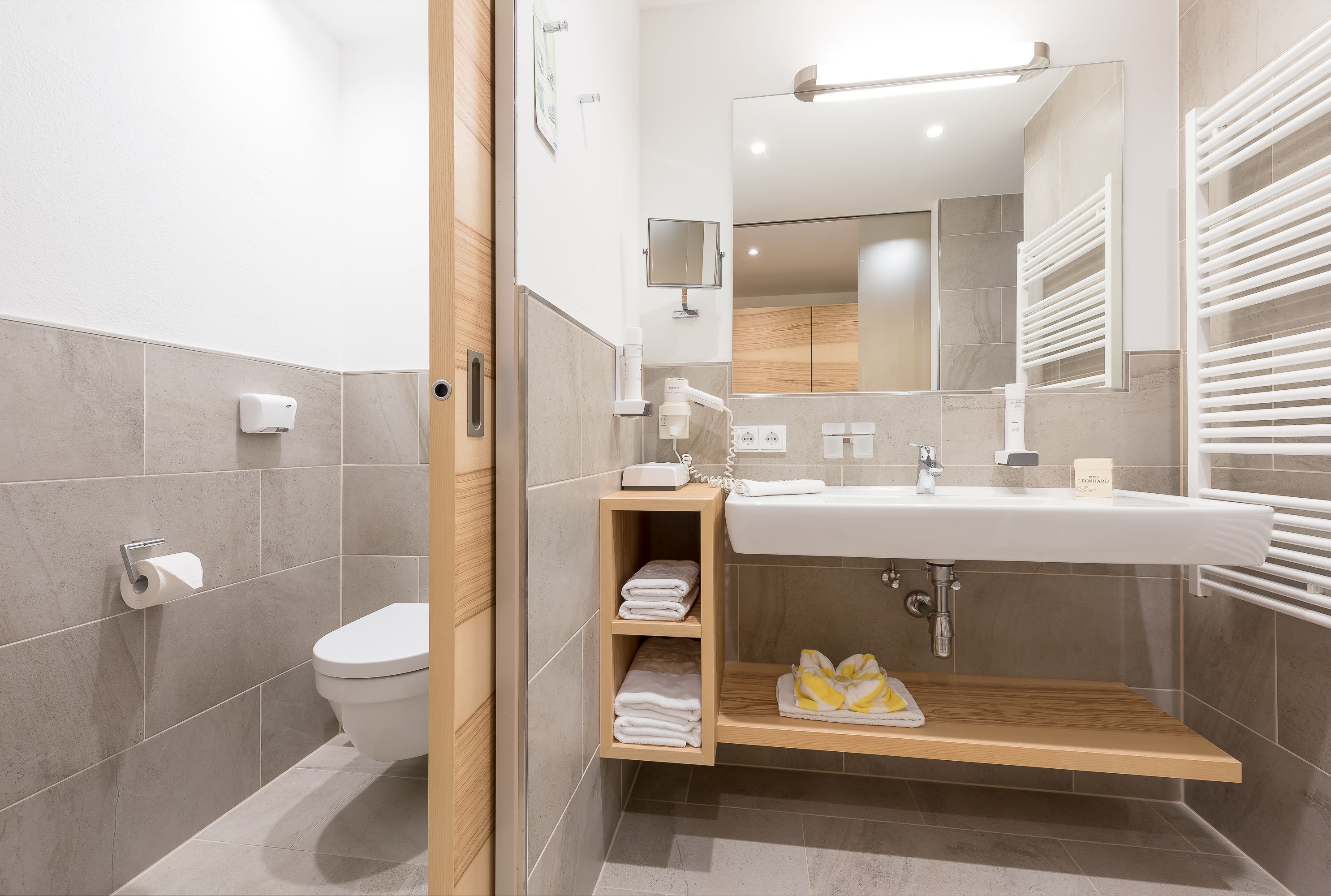Un baño moderno con inodoro, lavamanos y estantes empotrados para toallas.